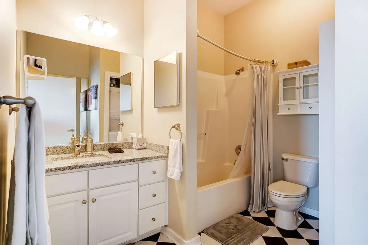 A fresh, spa-inspired bathroom scene with a granite countertop, black and white floor tiles, a large mirror, and a glimpse of the shower area. The space is bright, clean, and perfect for pampering routines, hinting at plush towels and relaxing moments.
