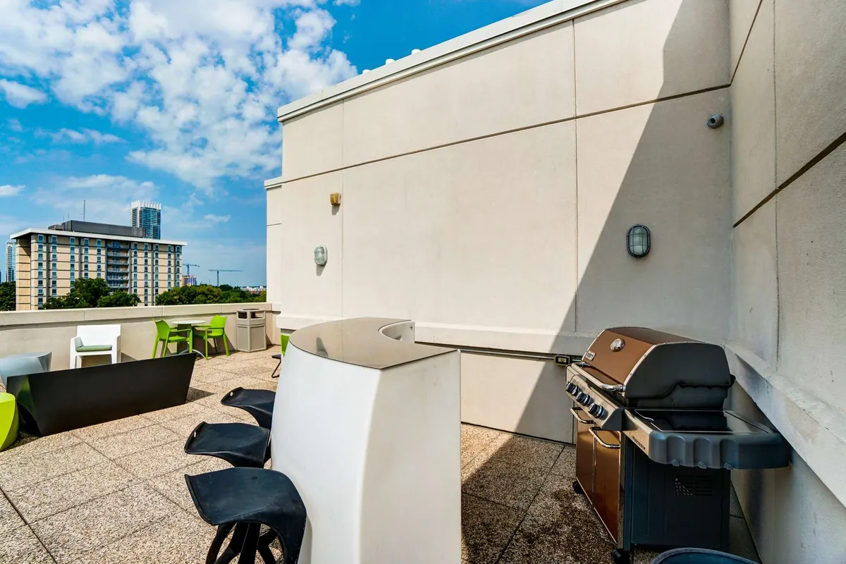 The image spotlights a modern outdoor area featuring a BBQ grill, bar-style seating, and chic outdoor furniture. The arrangement suggests a space designed for enjoyment—ideal for barbecuing, socializing, and relaxing in both intimate and festive settings.