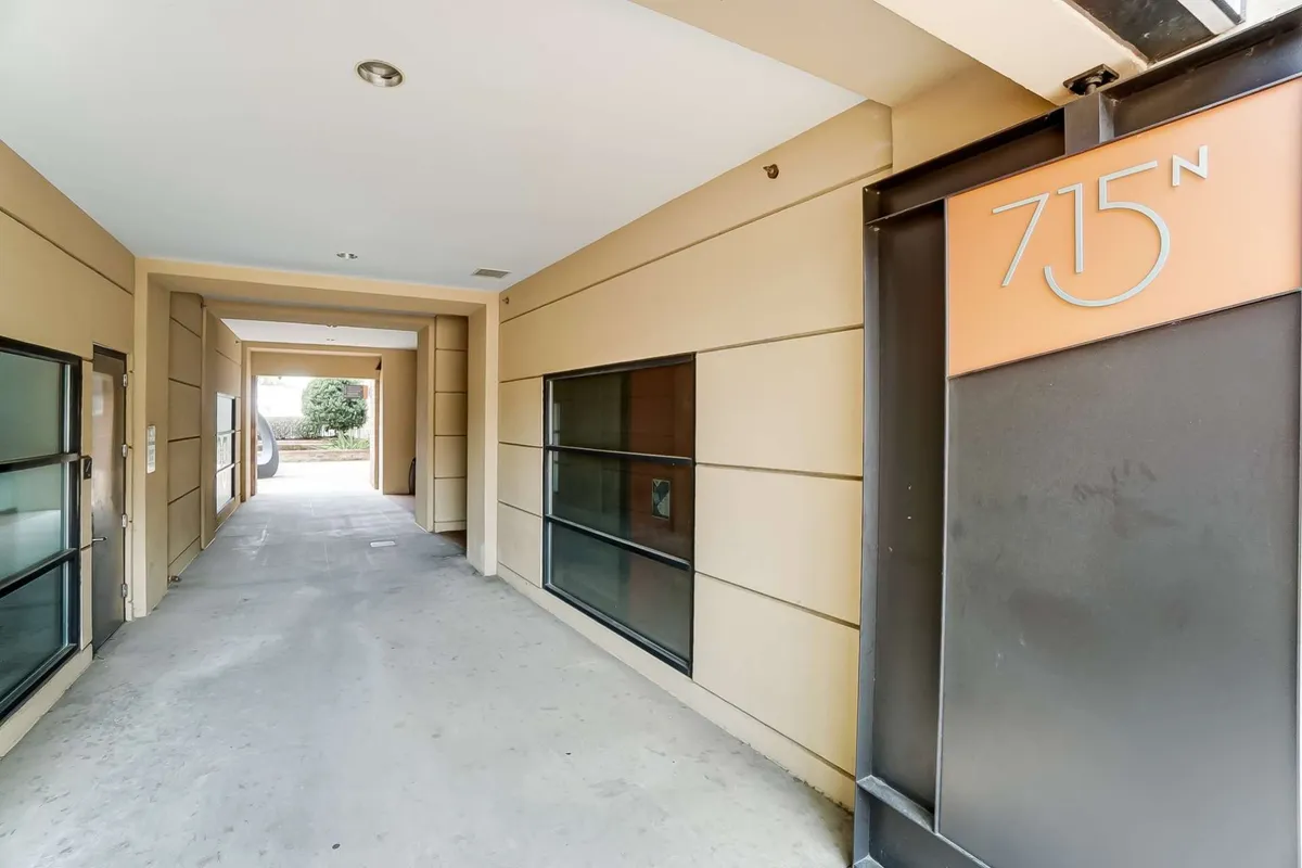 This image centers on the stylish entrance sign marked '715 N,' open corridors, and floor-to-ceiling glass windows, creating an impression of arrival and inviting access. The scene suggests a modern, energetic atmosphere where guests and residents mingle.