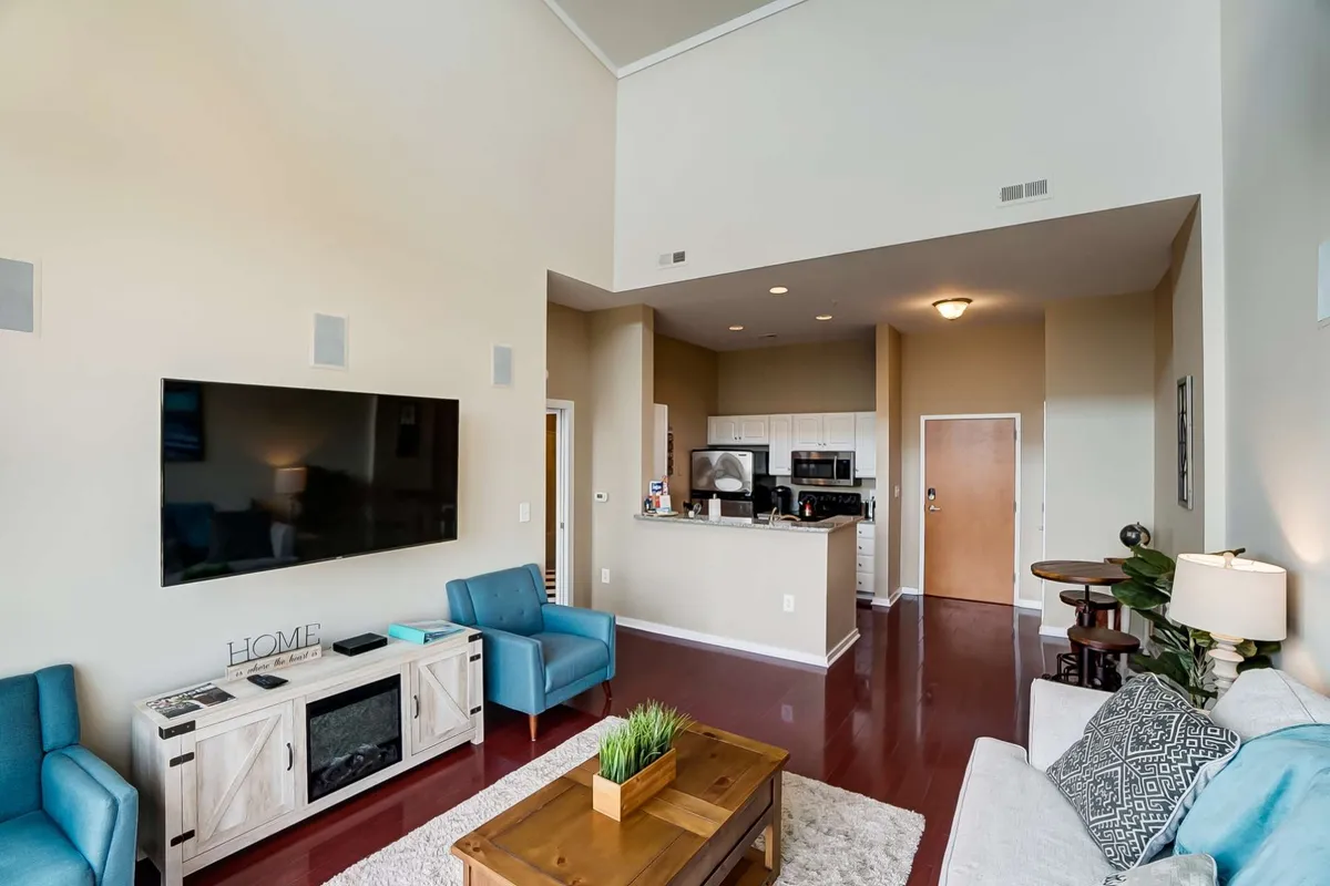 A cozy living area with a comfortable sofa, blue accent chairs, and a large flat-screen TV. The space feels inviting, with touches that suggest relaxation after city adventures. Decorative cushions and a coffee table with a plant add warmth and style.