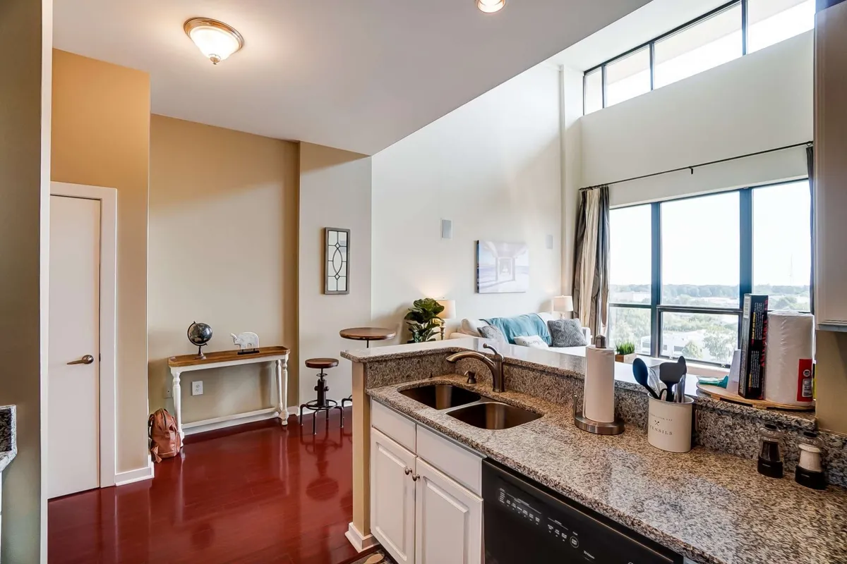 An open-concept living area that seamlessly connects the kitchen island, large windows, and the seating area. The room is styled with decorative wall art and modern furnishings, offering a bright, airy ambiance ideal for entertaining, relaxing, or enjoying breathtaking sunsets over the city.