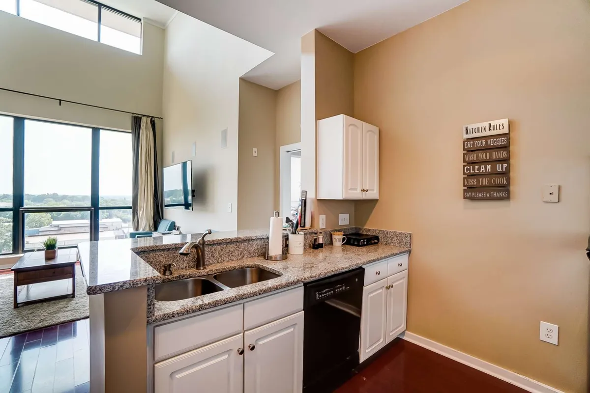 This modern kitchen highlights granite countertops and updated appliances, accompanied by large windows that let in natural light and offer city views. Decorative elements and open sightlines connect the kitchen to adjacent living and dining spaces.