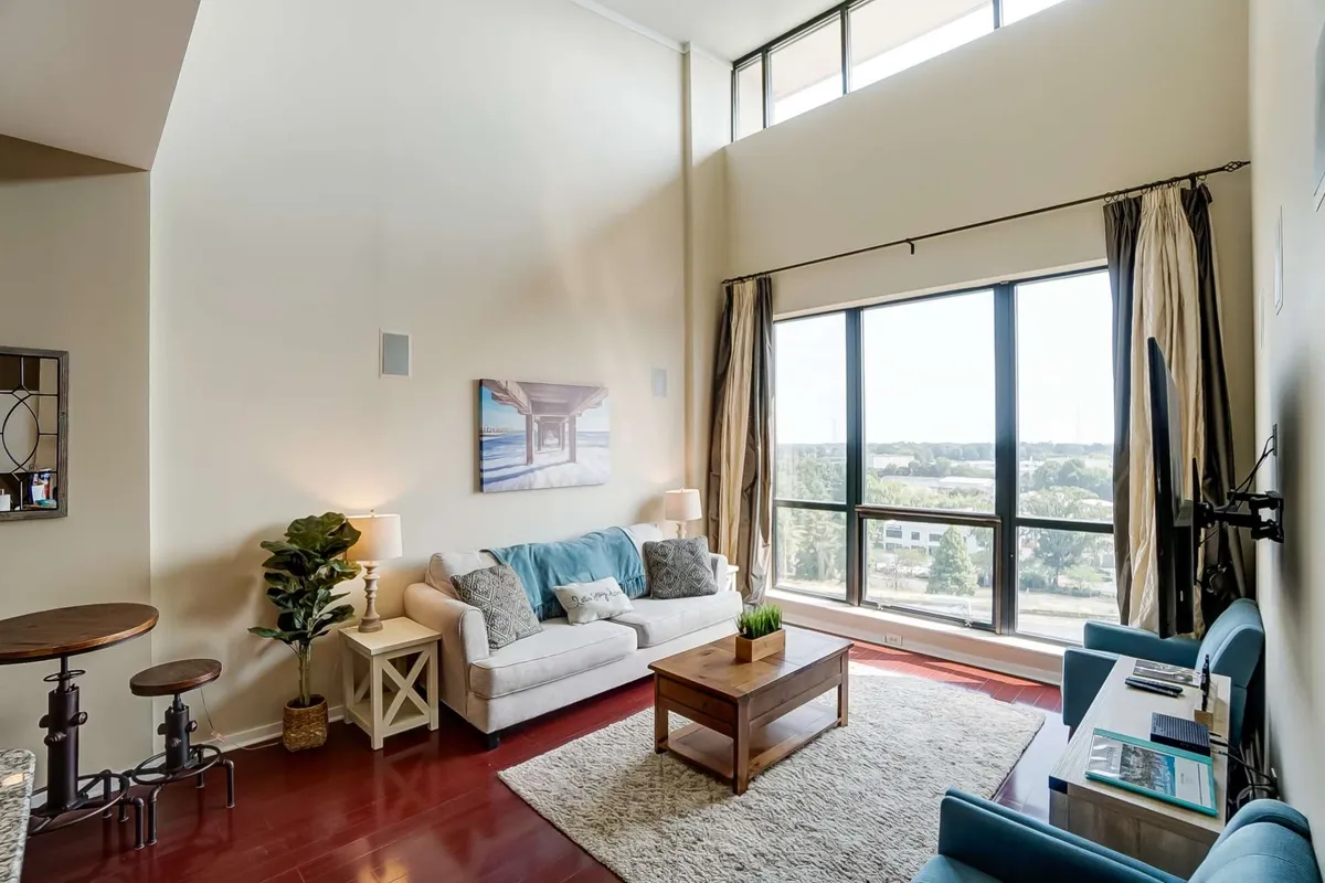 A spacious, inviting living area with a comfortable sofa, large windows letting in ample natural light, a coffee table, and vibrant artwork. The setting is perfect for relaxing, socializing, or enjoying a morning coffee while taking in city views.