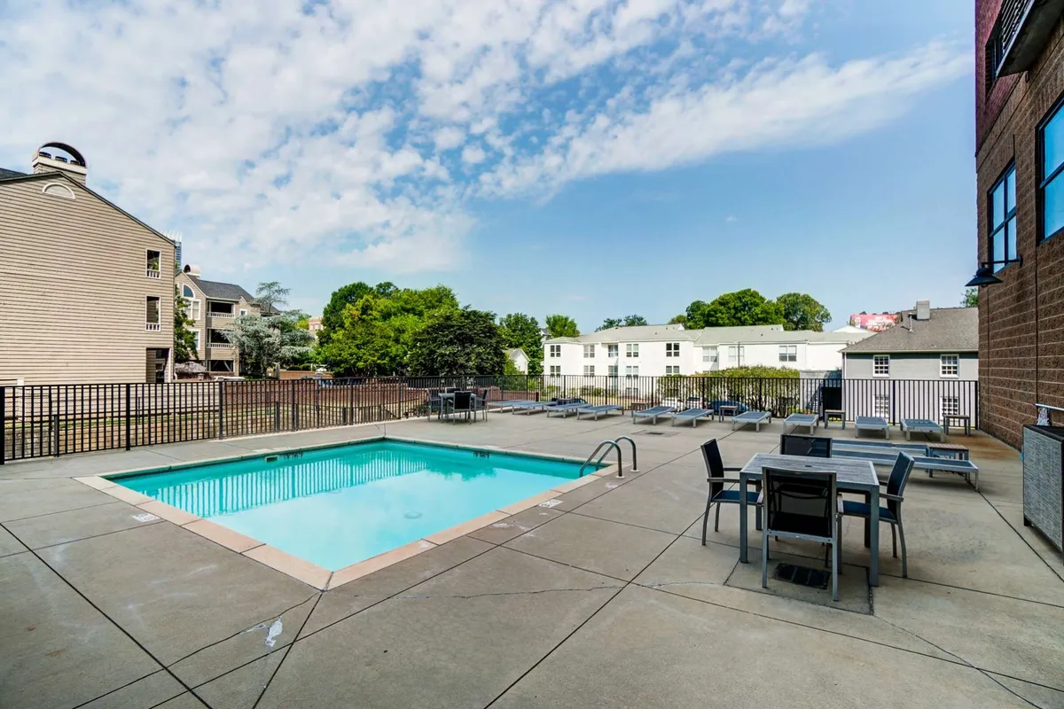 This image features a swimming pool set beside an outdoor dining area, framed by lush greenery. The space is designed for relaxation, sunbathing, and social gatherings, with comfortable seating and a tranquil atmosphere. The pool, central to the layout, is inviting and well-maintained, reflecting the light and enhancing the sense of a private, luxurious retreat.