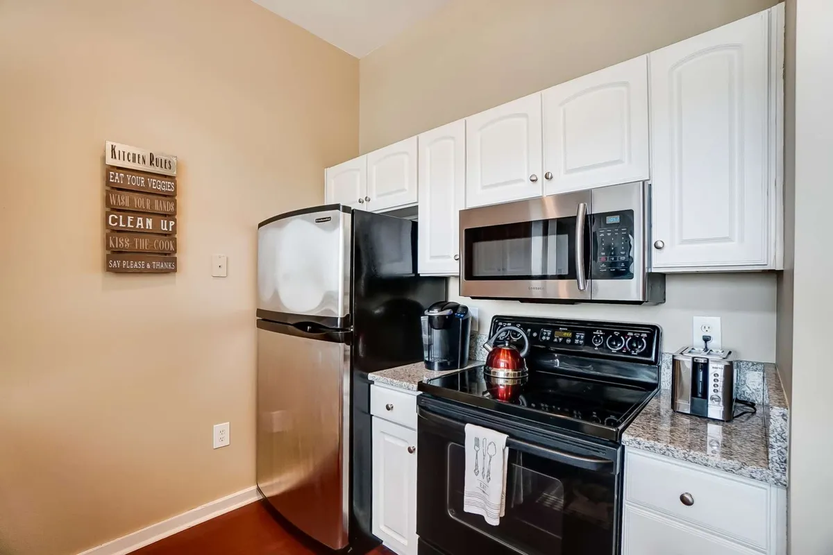 A warmly lit kitchen scene showcasing stainless steel appliances, granite countertops, and a decorative 'kitchen rules' sign. The design blends functionality with a welcoming atmosphere, hinting at shared family meals and gatherings.