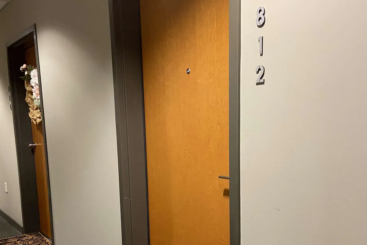 A well-lit hallway view featuring the door marked '812' and a neighboring door adorned with festive decorations. The entryway exudes a sense of arrival and welcome, linking the interior to the broader community and hinting at seasonal celebrations.