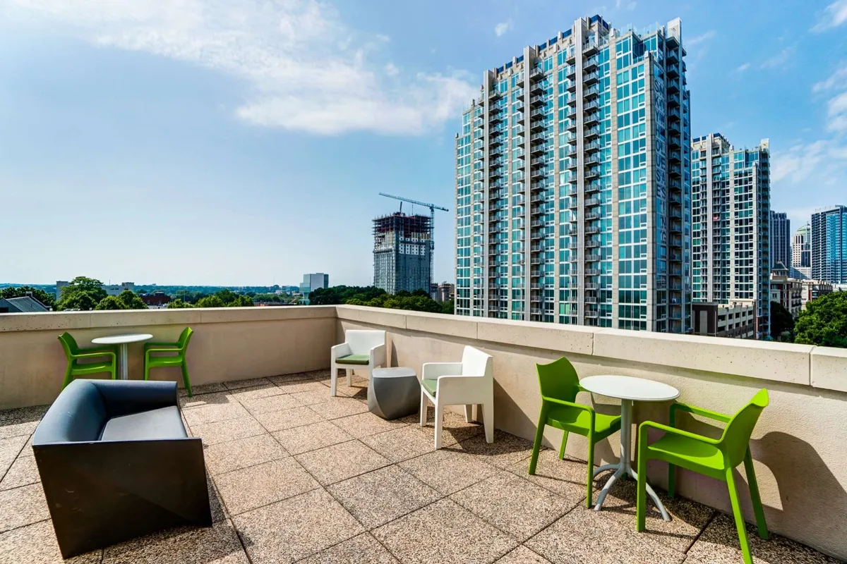 The image showcases a stunning rooftop terrace atop a modern penthouse, featuring sleek outdoor furniture arranged for relaxation and gatherings. The terrace offers panoramic views of Charlotte’s vibrant city skyline, with the sun setting in the background, creating a warm and inviting atmosphere perfect for socializing or unwinding. The space exudes a sophisticated, urban vibe, making it an ideal spot for enjoying coffee, cocktails, or simply soaking in the energy of Uptown.